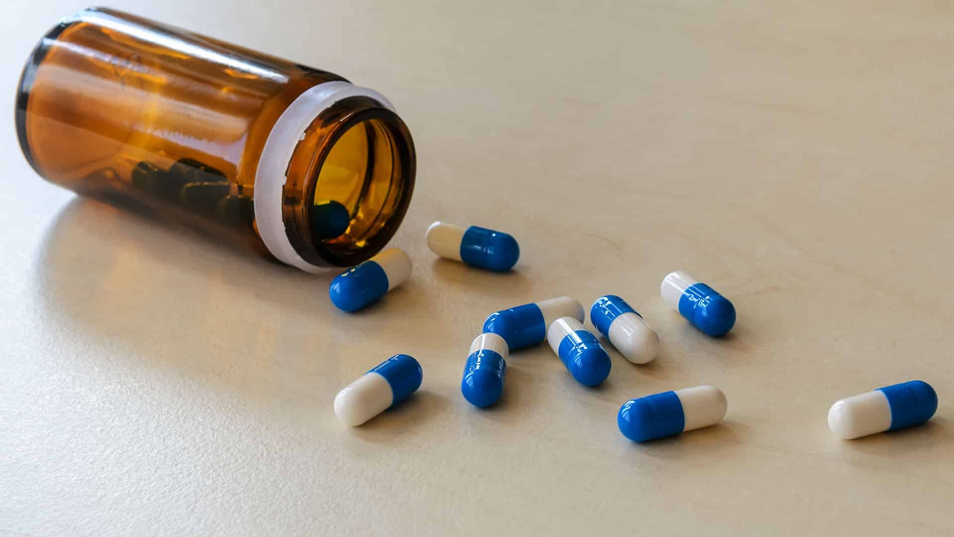 scattered pills and brown glass jar on a table