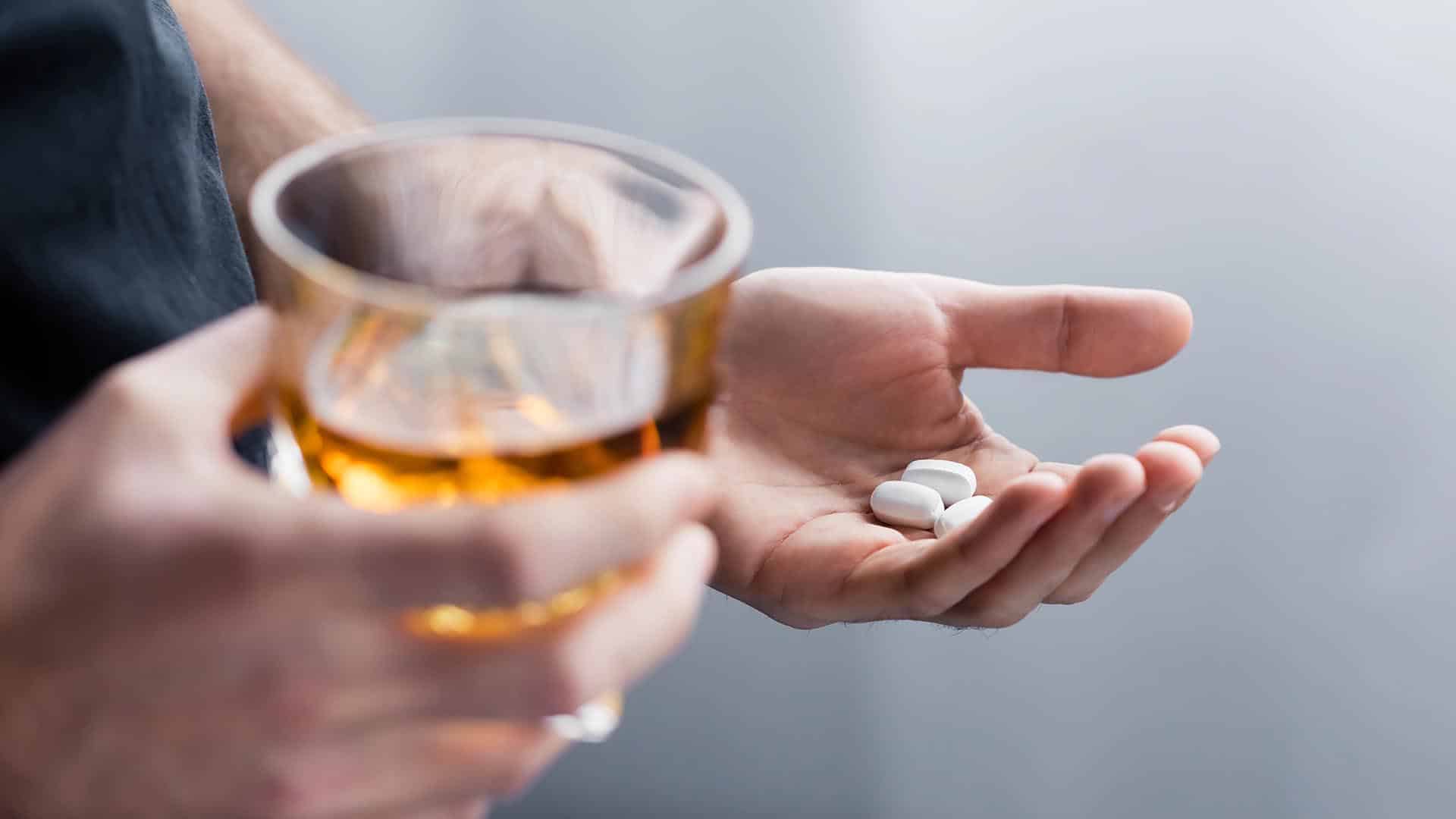 man holding handful pills glass whiskey