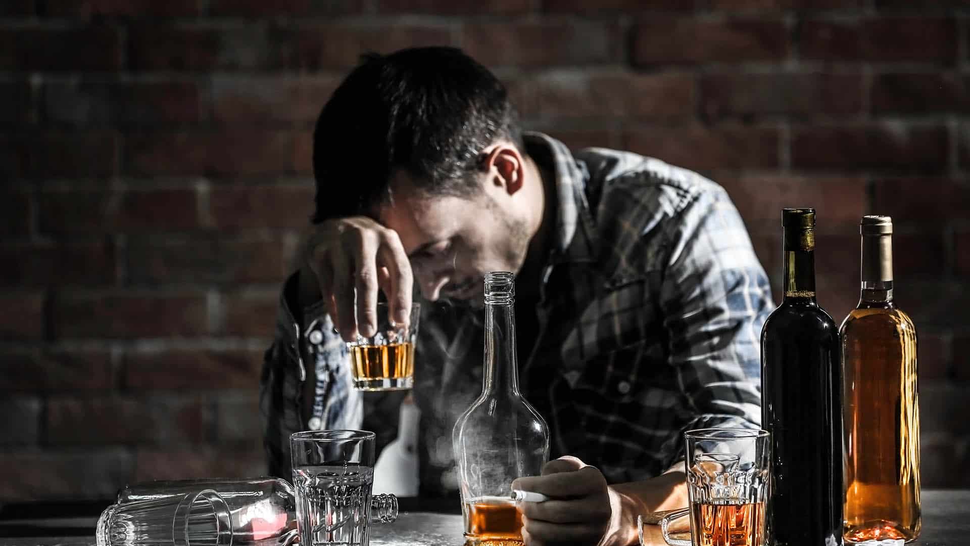 Drunk man with glass and bottles of alcohol