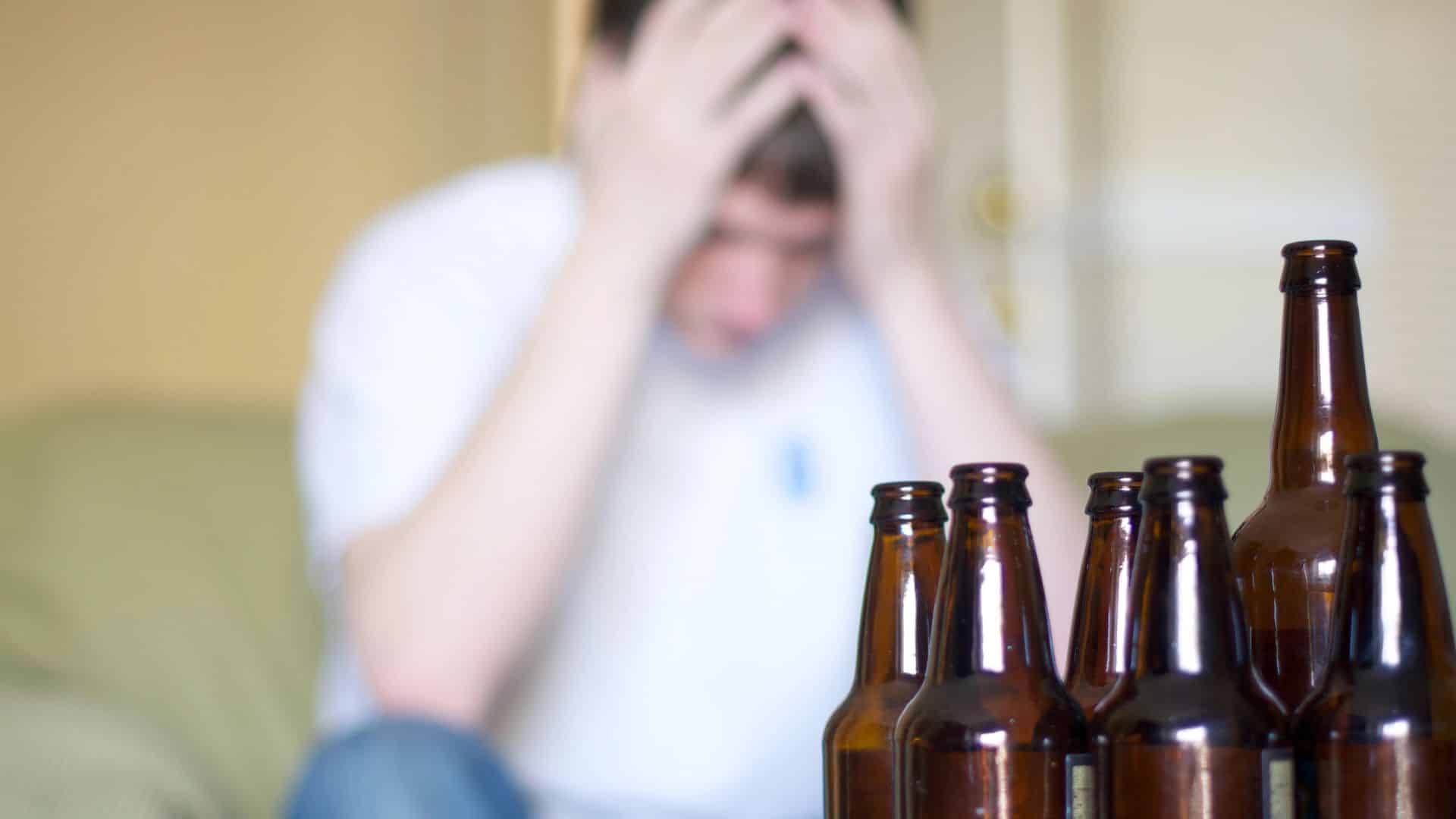 Man doing home detox holds head with group of empty beer bottles